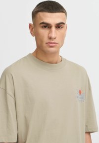 T-shirt en coton beige avec une coupe décontractée, doté de manches courtes et d'un col rond. Le design comprend un graphique coloré de soleil sur la poitrine gauche.