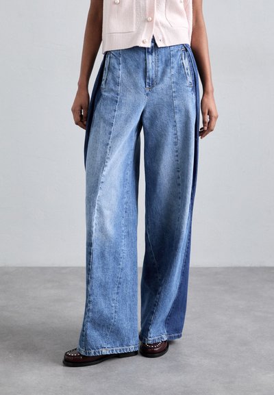 Light blue wide-leg jeans with contrasting dark blue paneling, featuring vertical zip accents, crafted from denim with a smooth texture.