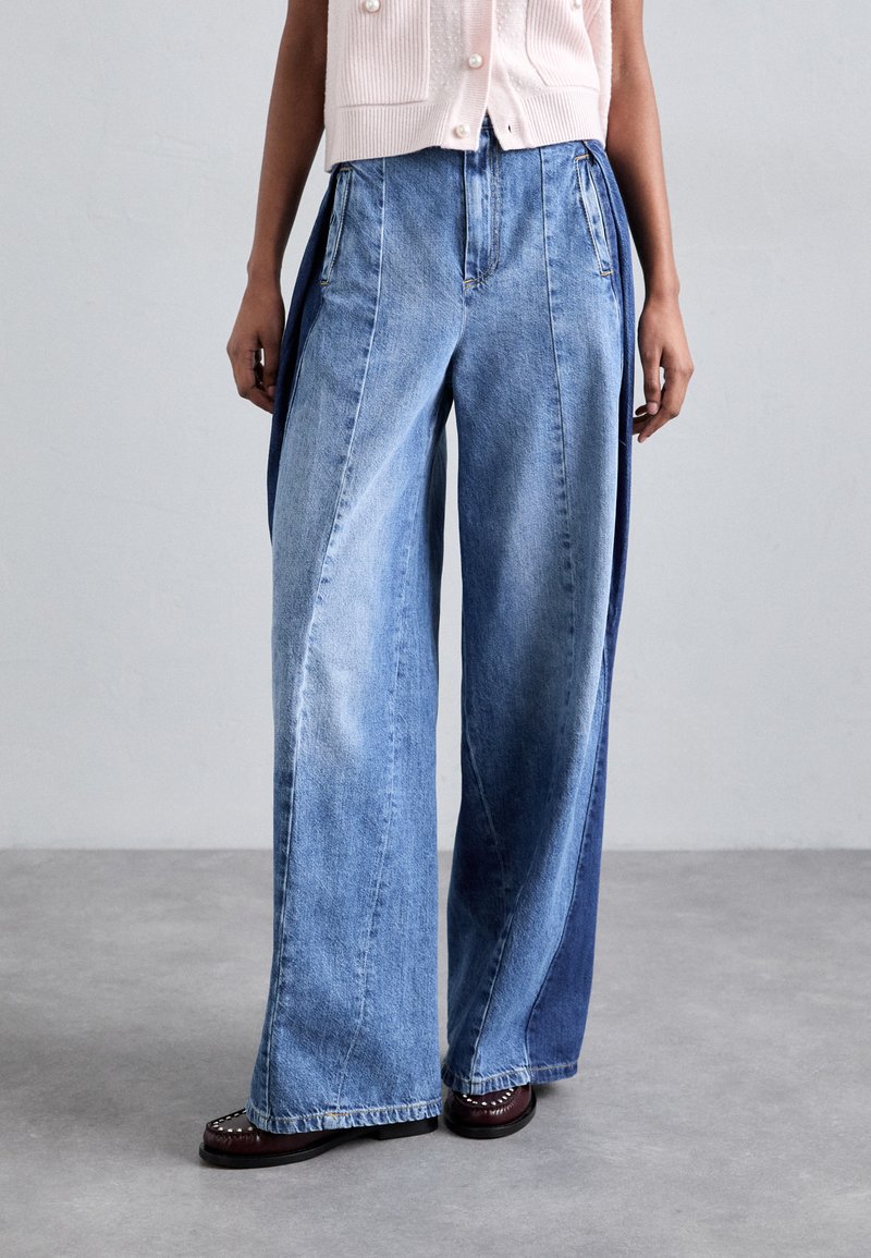 Lichtblauwe wijde jeans met contrasterende donkerblauwe panelen, voorzien van verticale ritssluitingen, gemaakt van denim met een soepele textuur.