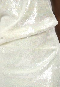 Witte sequined stof met een gestructureerd oppervlak, met een glanzende, iriserende uitstraling. De soepele val toont subtiele plooien en glans.