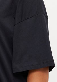 Svart bomull T-skjorte med kortermet design, synlige sømmer langs kanten og glatt tekstur.