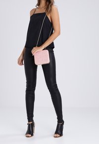 Top noir sans manches avec fines bretelles, leggings en simili cuir noir, et un sac carré à sequins rose clair avec une chaîne.