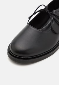 Black leather shoe with a rounded toe, lace-up design, textured upper, and a flat rubber sole with a subtle stitch detail.