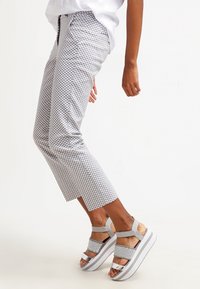 Szare, wzorzyste spodnie 3/4 z geometrycznym wzorem, w połączeniu z masywnymi sandałami na białej podeszwie i szarymi paskami.