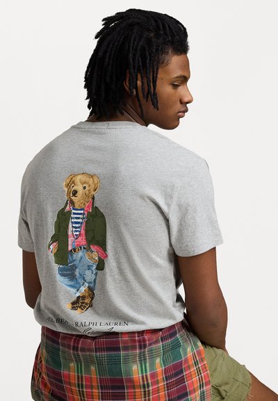 Szara bawełniana koszulka z ilustracją niedźwiedzia ubranego w zieloną kurtkę, koszulę w kratę i dżinsy. Poniżej znajduje się napis "Polo Bear Ralph Lauren."