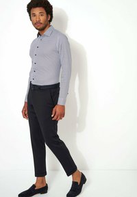 Langsleeve shirt in marineblauw met witte stippen, gecombineerd met fitted zwarte broeken en donkere loafers. Heeft een klassieke kraag en knoopsluiting.