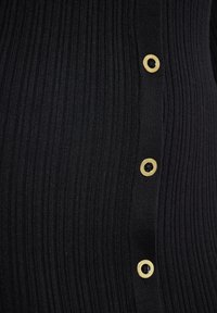 Haut en maille côtelée noire avec des boutons dorés le long du côté, présentation texturée verticale et coupe ajustée.