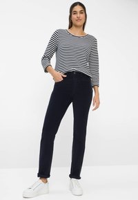 Gestreepte lange mouwen top in marineblauw en wit, gecombineerd met donkerblauwe broek. Model draagt witte sneakers. Eenvoudig ontwerp, casual pasvorm en opgerolde manchetten.