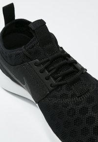 Svarta sneakers med nätövre, texturerat tyg och helt svarta accenter. Har en snörningsdesign och en vit sula.