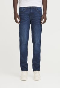 Jeans iz jeansa v temno modri barvi s ravnimi hlačnicami, petimi žepi, subtilno obrabljenim izgledom in srednje visokim pasom, v kombinaciji z belimi supergami.