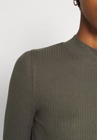 Top a coste di colore verde oliva con un collo alto e una silhouette aderente, caratterizzato da una consistenza morbida e un sottile lucido.