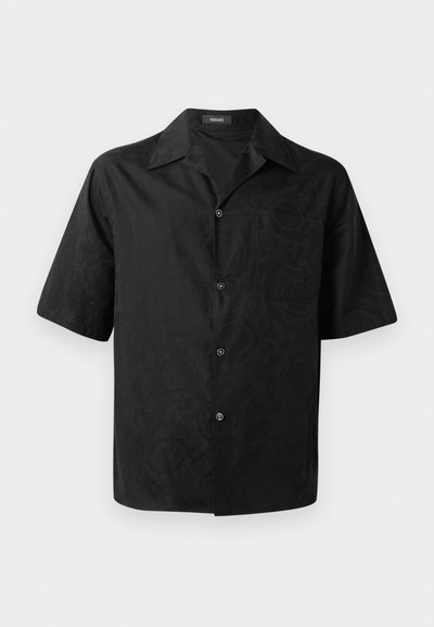 Chemise noire à manches courtes avec un motif floral texturé subtil, fermeture éclair à boutons, col et poche sur la poitrine gauche. Fabriquée en tissu léger.