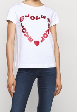 Biała koszula z krótkim rękawem z czerwonym brokatowym tekstem tworzącym kształt serca z napisem "LOVE" oraz symbolami słońca i serca, noszona z ciemnoniebieskimi jeansami.