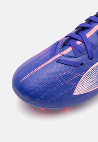 Scarpe da calcio viola con accenti rosa, tomaia in sintetico testurizzato, punta rotonda e chiusura con lacci. Caratterizzate da motivi geometrici e suola rigida.