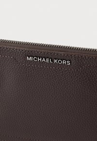 Barna, texturált bőr kézitáska ezüst cipzárral és "MICHAEL KORS" logóval ezüst színben. Kontrasztos varrással díszített a szélek mentén.