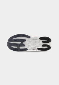 Λευκή και μαύρη σόλα αθλητικού παπουτσιού με υφασμένους μοτίβα πιασίματος σε απλό ανοιχτό γκρι φόντο.