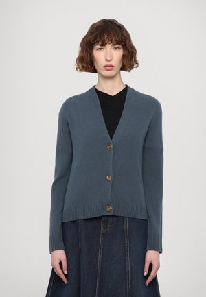 Blauer Strickcardigan mit V-Ausschnitt, fünf Knöpfen und geripptem Saum. Kombiniert mit einem schwarzen Oberteil und einem Jeansrock, vor einem neutralen Hintergrund gezeigt.