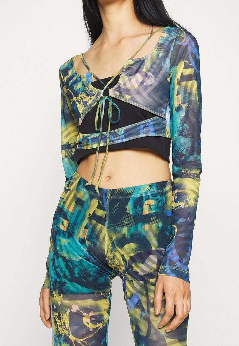 Bunt gemustertes Crop-Top und Leggings-Set aus transparentem Stoff mit abstrakten Mustern in Blau, Grün und Schwarz, mit Bindeakzenten.