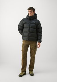 Black puffer jacket with a hood, quilted texture, paired with brown cargo pants, worn with green hiking shoes.