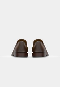 Scarpe in pelle marrone con una superficie liscia, punta arrotondata e tacco basso e robusto. Il design presenta una silhouette minimalista e una cucitura discreta.