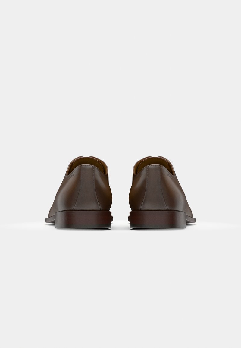 Chaussures en cuir marron avec une texture lisse, bout arrondi, et un talon bas et robuste. Le design présente une silhouette minimaliste et des coutures discrètes.
