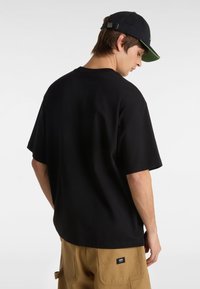 Schwarzes Baumwoll-T-Shirt mit kurzen Ärmeln und lässigem Schnitt, kombiniert mit beigen Arbeitshosen, die Taschen und ein Etikett auf der Rückseite haben.