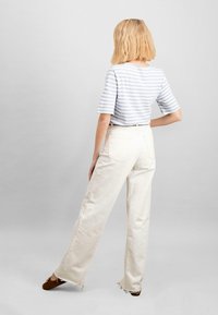 Prúhovaný svetlomodrý a biely skrátený top v kombinácii s off-white rovným strihom nohavicami s potrhnutými lemami a zadnými vreckami. Hnedé nazúvacie topánky.