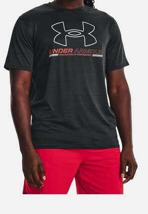 Mann trägt schwarzes Under Armour T-Shirt mit Logo und rote Shorts, steht mit entspannten Armen an den Seiten.