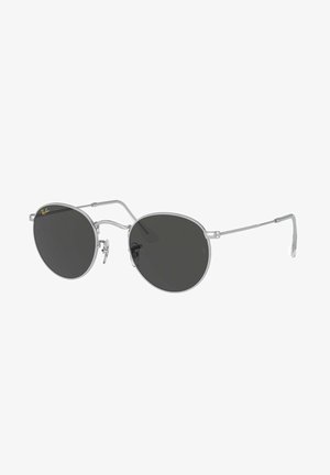 Occhiali da sole con una sottile montatura in metallo argentato, lenti scure di forma rotonda, supporti per il naso regolabili e un design minimalista. Logo Ray-Ban vicino alla lente.