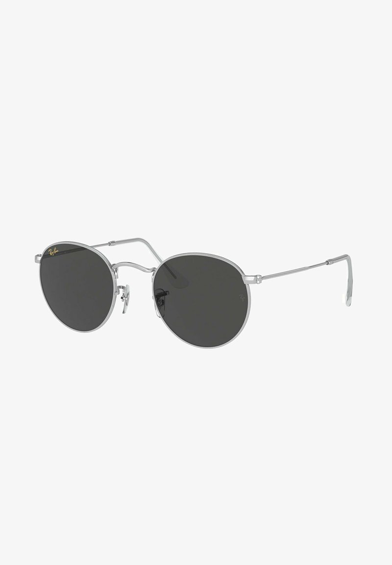 Occhiali da sole con una sottile montatura in metallo argentato, lenti scure di forma rotonda, supporti per il naso regolabili e un design minimalista. Logo Ray-Ban vicino alla lente.