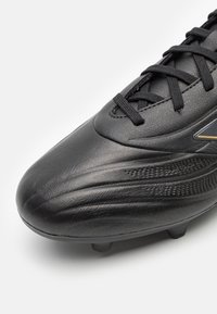 Black soccer shoe featuring a textured synthetic upper, molded studs, and a sleek design with subtle gold accents.