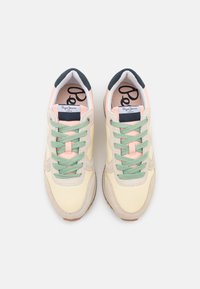 Tenisky se světle žlutým svrškem, zelenými tkaničkami, béžovými semišovými doplňky a tmavě modrým páskem na patě. Na jazyku je logo.