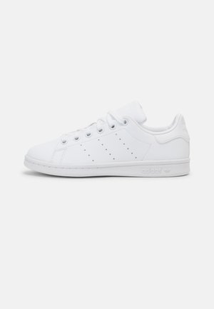 Baskets basses blanches Adidas avec trois bandes perforées, fermeture à lacets et semelle de marque, vues de côté sur fond uni.