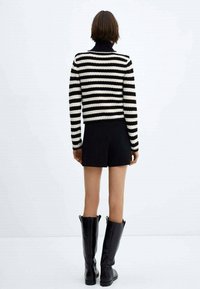 Gestreifter Pullover in Schwarz-Weiß mit hohem Kragen, kombiniert mit schwarzen Shorts und knielangen schwarzen Stiefeln. Glatte Oberfläche und taillierte Passform.