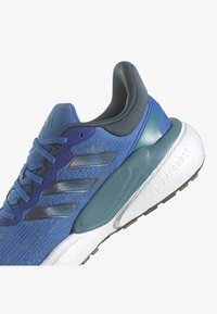 Blå löparsko med svarta ränder, vadderad svart krage, vit texturerad sula märkt "Lightboost" och blå vadderad mellansula.