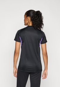 Μαύρη αθλητική μπλούζα με κοντά μανίκια, διακοσμημένη με μωβ λεπτομέρειες στους ώμους, από απαλό ύφασμα και εφαρμοστή σχεδίαση.