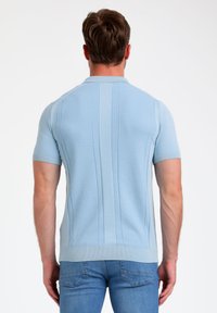 Camisa polo de manga corta azul claro con cuello acanalado y textura de rayas verticales, combinada con jeans azul claro.