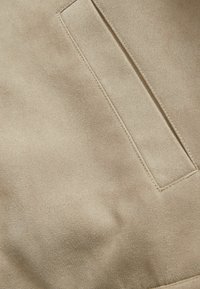 Țesătură de suede bej cu o textură netedă; are un buzunar rectangular aplicat și cusături vizibile care conturează buzunarul.