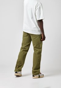 Olijfgroene cargobroek met meerdere opgestikte zakken, rechte pijpontwerp, gemaakt van duurzaam katoen. Gedirigeerd met een wit T-shirt en sneakers.
