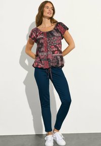 Top a maniche corte nero e bordeaux con motivo, vita stretta e dettaglio con cordino, abbinato a pantaloni skinny blu e sneakers bianche.