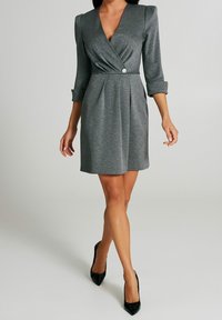Szara sukienka z długim rękawem, z głębokim dekoltem w kształcie litery V, plisowanym przodem i srebrnym detalem z guzikami. Wykonana z miękkiego materiału, kończy się powyżej kolana.