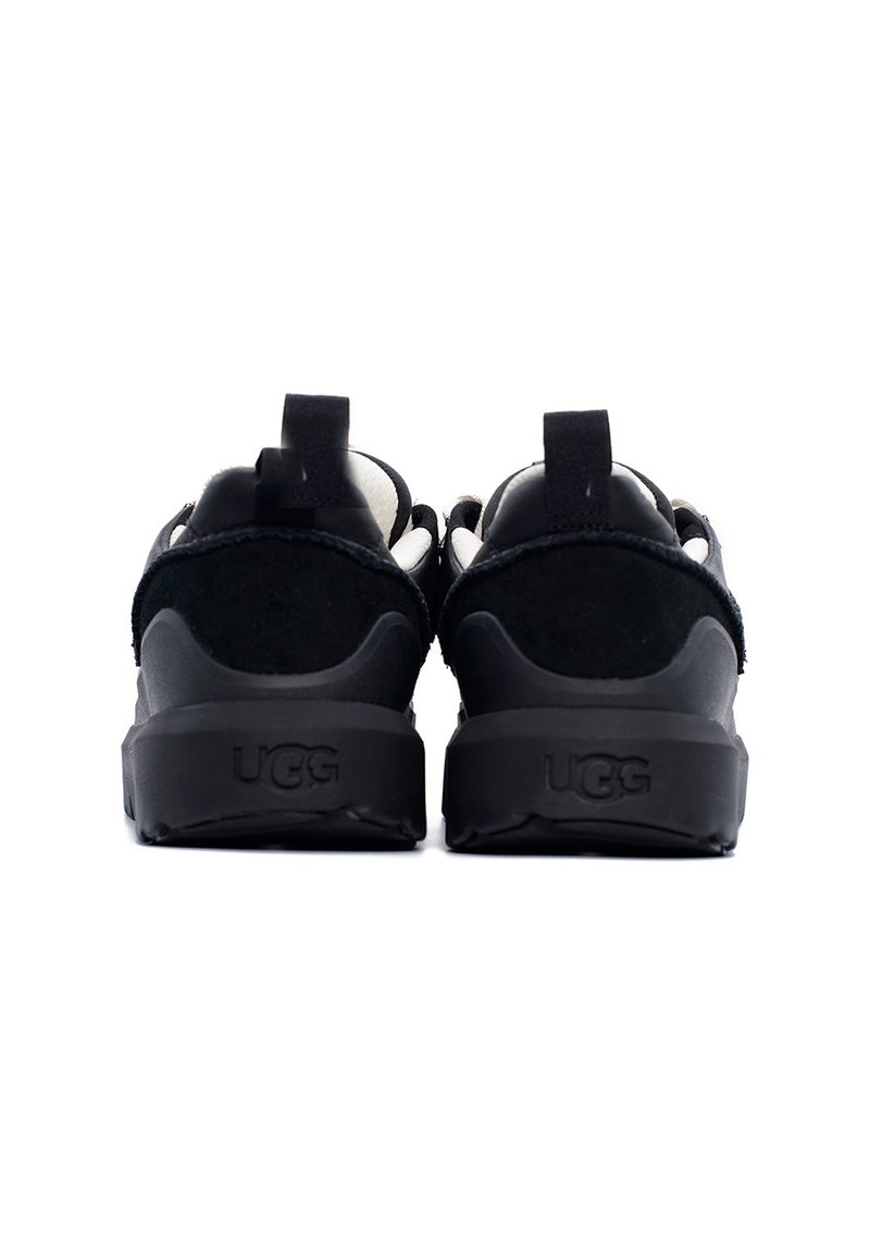 Zwarte suede en synthetische achterkant van UGG-schoenen met een gevoerde zool, lus voor gemakkelijke instap en textuurdetail langs de bovenkant.