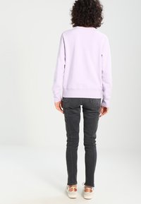 Lila sweatshirt med rund hals och långa ärmar, tillsammans med mörkgrå slim-fit-jeans. Avslappnade sneakers fulländar outfiten.