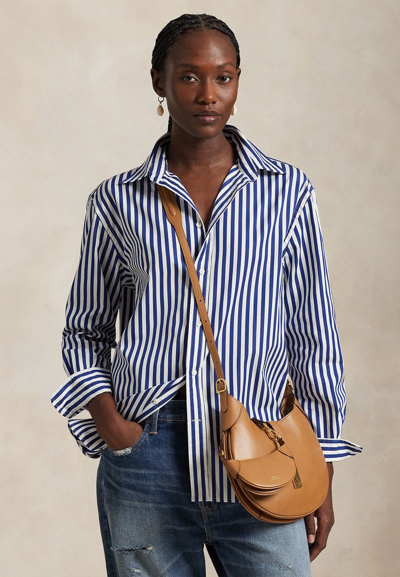 Camicia a righe bianche e azzurre con bottoni e maniche lunghe, abbinata a una borsa a tracolla in pelle color cuoio con chiusura a scatto e cinturino regolabile.