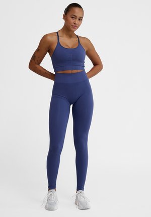 Navy Sport-BH und hochtaillierte Leggings aus geripptem Material; mit Trägern und einem strukturierten Bund; kombiniert mit hellgrauen Sneakern.