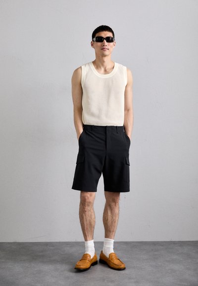 Valge ribadega tank top, mustad cargo-lühikesed püksid ja oranžad palmikkingad valgete sokkidega. Lihtne disain, ühtsed värvid ja funktsionaalsed taskud.