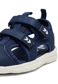Navy blue sandal with mesh upper and synthetic straps. Features Velcro fasteners and a white rubber sole with a textured tread pattern.