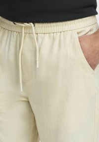 Beige joggerbukser med elastisk talje, snøre og sidelommer. Stoffet synes Let og har en subtil tekstur.