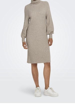 Abito a maglia beige a coste con colletto alto e maniche a palloncino, che termina sopra il ginocchio. Abbinato a sneakers bianche per un look informale.
