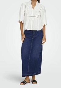 Vit broderad blus med korta ärmar, kombinerad med en lång mörk denimkjol. Svarta sandaler med remmar fulländar outfiten.